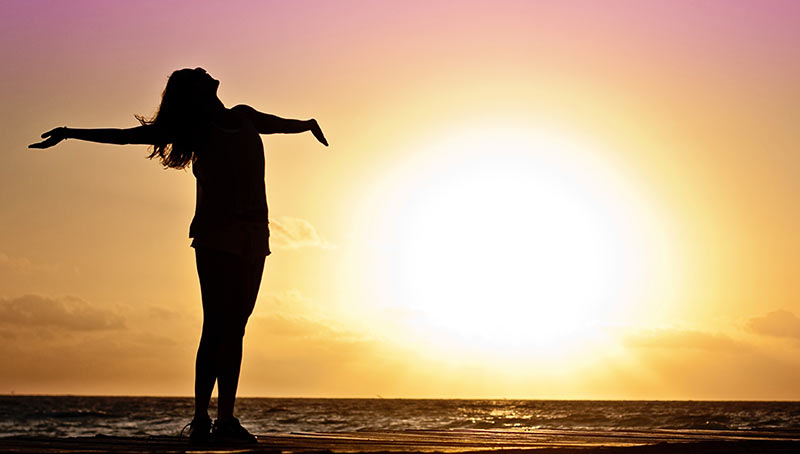 Silhouette einer Frau mit offenen Armen am Strand bei Sonnenuntergang als Symbol für Freiheit, Lebensfreude und Wohlbefinden durch aktive Mobilität Silhouette einer Frau mit offenen Armen am Strand bei Sonnenuntergang als Symbol für Freiheit, Lebensfreude und Wohlbefinden durch aktive Mobilität