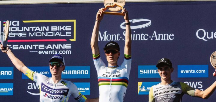 Finn Treudler jubelt beim Cube Factory Racing Saisonfinale 2025 in Mont-Sainte-Anne mit der Trophäe in den Händen, flankiert von dem Zweit- und Drittplatzierten auf dem Podium.
